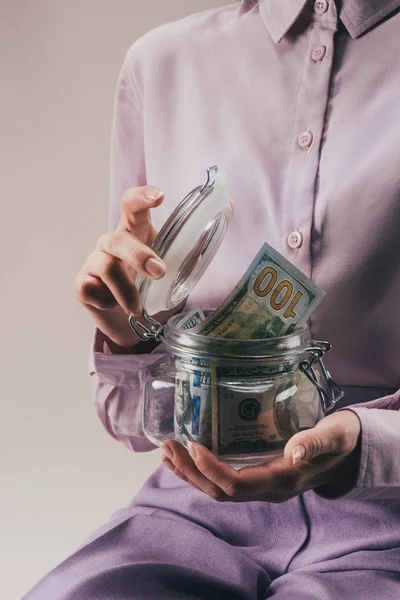 Vista parziale di donna in possesso di vaso di vetro con risparmi isolati su lilla — Foto stock