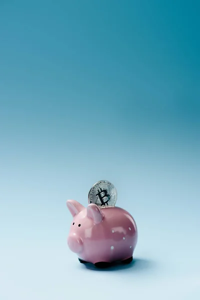 Close up view of pink piggy bank and silver bitcoin on blue backdrop — Stock Photo