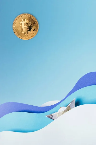 Vue rapprochée du bitcoin doré et du bateau en papier naviguant sur des vagues en papier bleu isolé sur bleu — Photo de stock