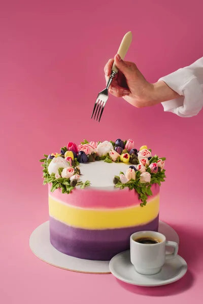 Plan recadré de femme avec fourchette, tasse de café et gâteau décoré de fleurs crème isolées sur rose — Photo de stock