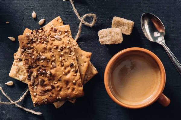 Vista dall'alto di biscotti, tazza di caffè, cucchiaio e zucchero di canna su un tavolo scuro — Foto stock