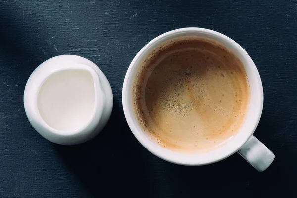 Vista dall'alto di tazza di caffè e jag di crema su un tavolo scuro — Foto stock