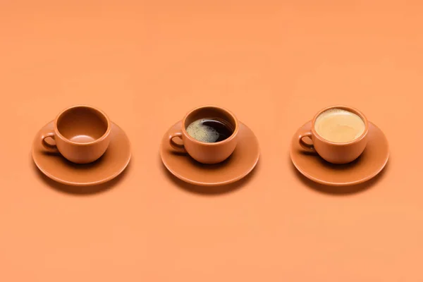 Close up view of arrangement of empty cup and two cups of coffee isolated on peach — Stock Photo