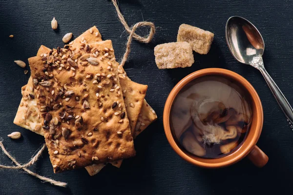 Vista dall'alto di biscotti, tazza di caffè, cucchiaio e zucchero di canna su un tavolo scuro — Foto stock
