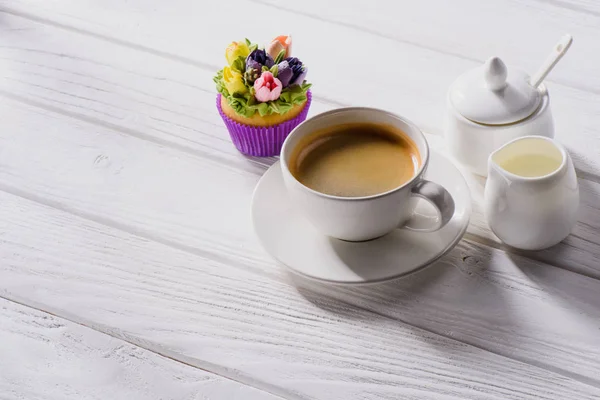 Close up view of cup of coffee, sweet muffin and jag of cream on white wooden tabletop — Stock Photo