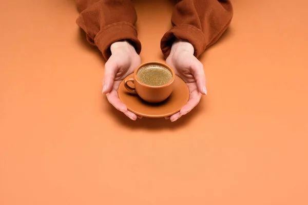 Abgeschnittene Aufnahme einer Frau, die Tasse Kaffee auf Untertasse in den Händen hält, isoliert auf Pfirsich — Stockfoto