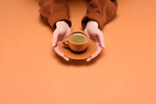 Plan recadré de femme tenant une tasse de café sur la soucoupe dans les mains isolées sur la pêche — Photo de stock