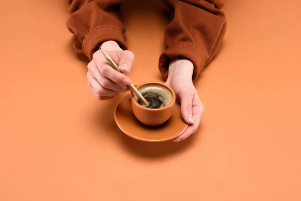 Partial view of female hands with cup of coffee and pencil isolated on peach — Stock Photo