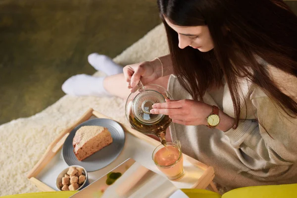 Aus der Vogelperspektive: Frau gießt zu Hause heißen Tee in Tasse auf Holztablett — Stockfoto