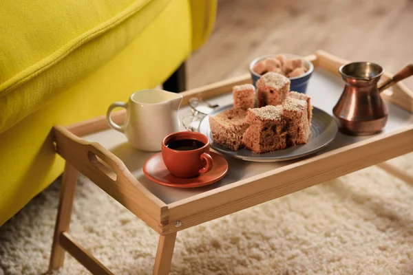 Vue rapprochée de tasse de café, jag de crème, morceaux de gâteau et cassonade sur plateau en bois dans la chambre — Photo de stock