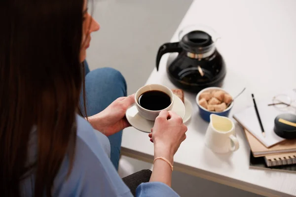 Vista parcial de la mujer con taza de café y mesa de café con cafetera, jag de crema y azúcar morena - foto de stock