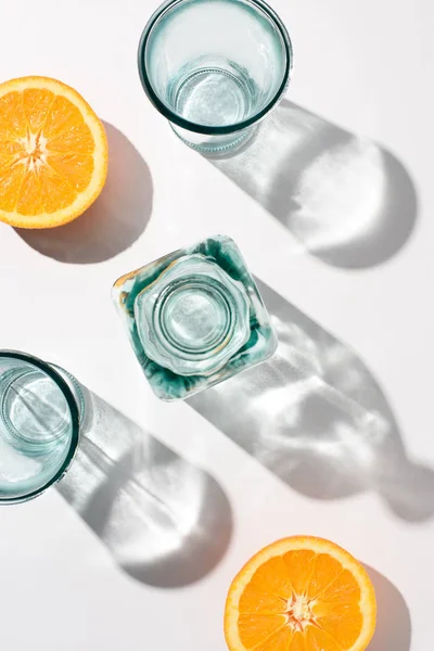 Vista superior de piezas de naranja, botella y vasos vacíos en la superficie blanca - foto de stock