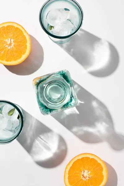 Vue de dessus des morceaux d'orange, bouteille et verres avec glace sur la surface blanche — Photo de stock