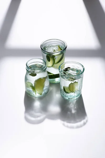 Vue rapprochée des verres avec de l'eau, des morceaux de citron vert et des glaçons sur la table blanche — Photo de stock