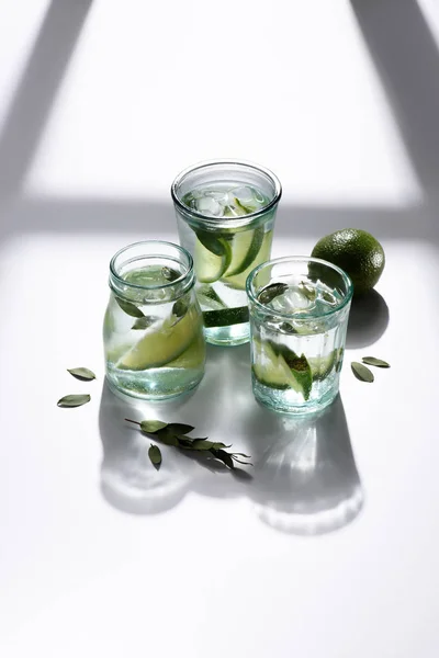 Vue rapprochée des verres avec de l'eau, des morceaux de citron vert et des glaçons sur la table blanche — Photo de stock