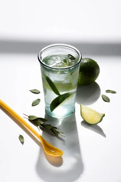 Nahaufnahme von Plastiklöffel, Glas Wasser mit Limettenstücken und Eis auf weißer Tischplatte — Stockfoto