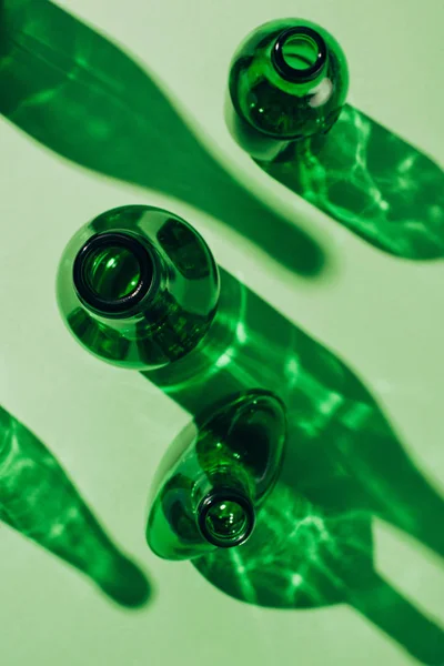 Vista superior de botellas de vidrio verde vacías arregladas con sombras en la mesa - foto de stock