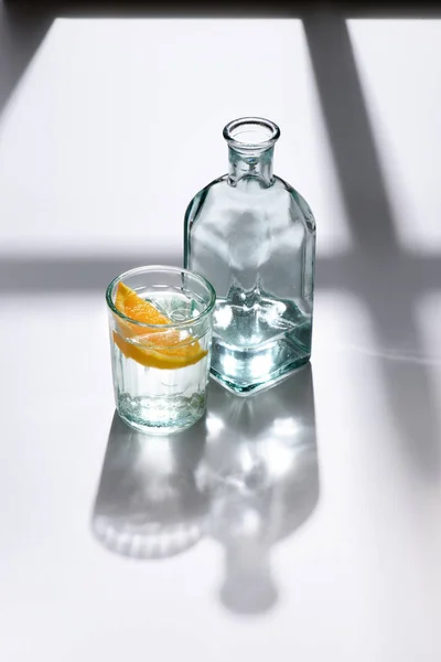 Close up view of glass with lemon piece and bottle with water on white surface — Stock Photo