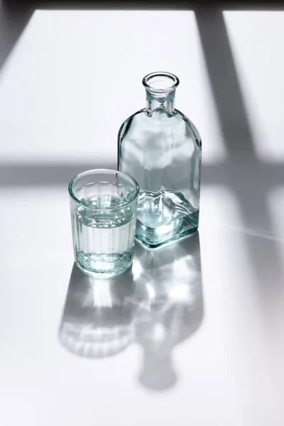 Primer plano vista de vidrio y botella con agua en la superficie blanca - foto de stock