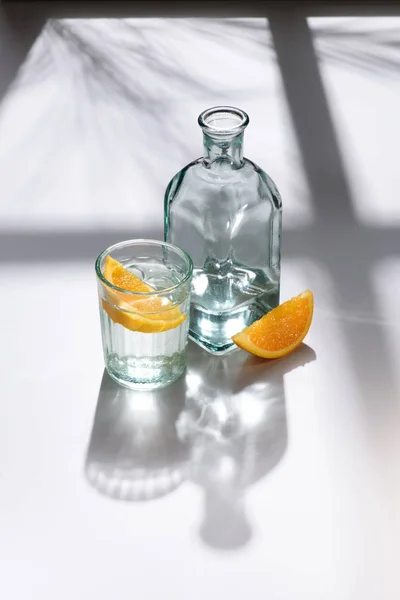 Close up view of glass, lemon pieces and bottle with water on white surface — Stock Photo