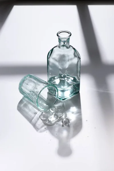 Vue rapprochée du verre vide et de la bouteille avec de l'eau sur la surface blanche — Photo de stock