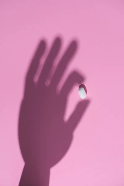 Vue du dessus de l'ombre de la main tenant la pilule sur la surface rose — Photo de stock