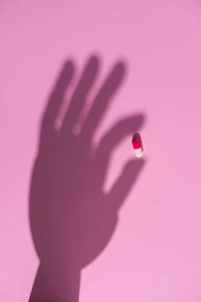 Вид зверху тіні руки, що тримає препаратну капсулу на рожевій поверхні — стокове фото