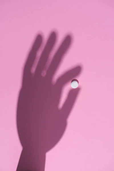 Vista superior da sombra da mão segurando pílula branca na superfície rosa — Fotografia de Stock