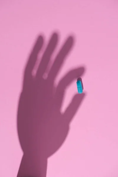 Вид сверху на тень руки с голубой таблеткой на розовой поверхности — Stock Photo