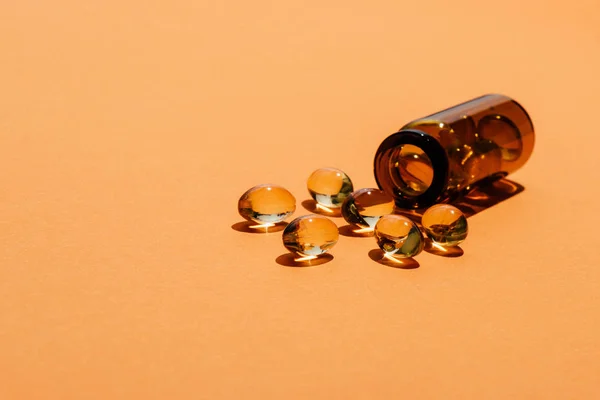Tiro close-up de comprimidos amarelos transparentes derramados da garrafa na superfície laranja — Fotografia de Stock