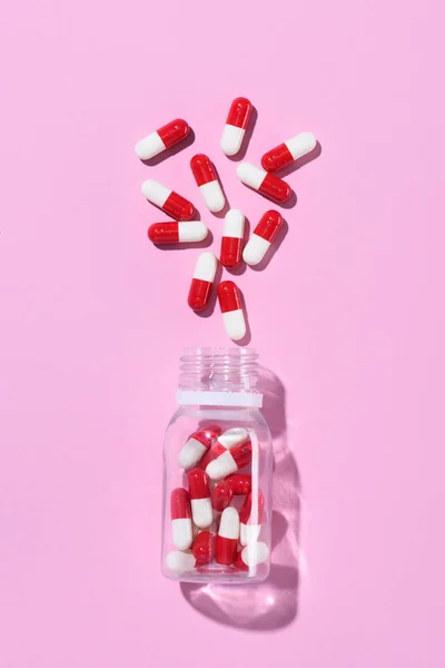 Vista superior de pílulas vermelhas derramadas de frasco de plástico em rosa — Fotografia de Stock