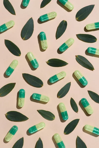 Vista dall'alto di pillole di fitoterapia con motivo di foglie verdi sulla superficie beige — Foto stock