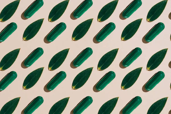 Ansicht von Phytotherapie-Kapseln mit grünen Blättern im Reihenmuster auf beiger Tischplatte — Stockfoto
