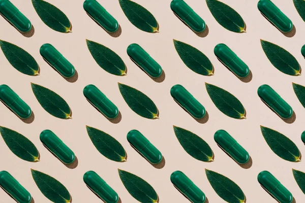 Vue du dessus des pilules de phytothérapie avec des feuilles vertes en rangées motif sur la surface beige — Photo de stock