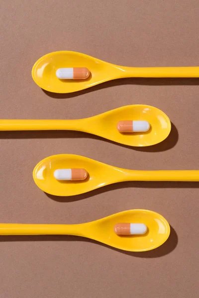 Vista superior de pílulas em colheres de plástico amarelo em marrom — Fotografia de Stock