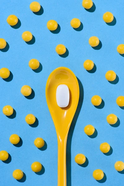 Top view of yellow plastic spoon with white pill surrounded with pills on blue — Stock Photo