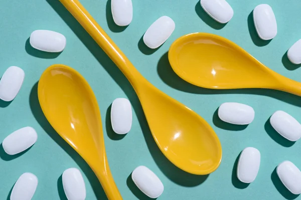 Vue du dessus des cuillères en plastique jaune entourées de pilules sur le dessus de table bleu — Photo de stock