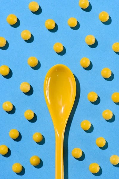 Vue du dessus de la cuillère en plastique jaune entourée de pilules sur bleu — Photo de stock
