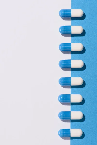 Vista superior de la fila de cápsulas de medicamentos en la mitad de la superficie blanca y azul - foto de stock