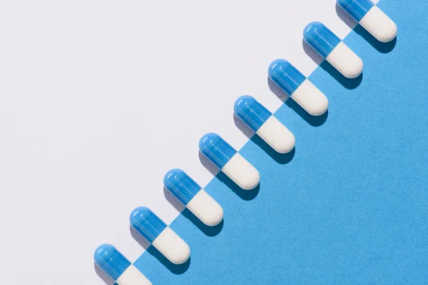 Vista dall'alto di fila di pillole sulla superficie bianca e blu dimezzata — Foto stock
