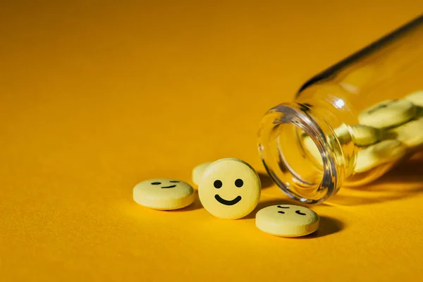 Gros plan des pilules avec des visages souriants et bouteille en verre sur jaune — Photo de stock