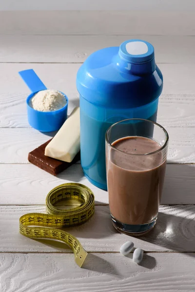 Chocolate protein shake with measuring tape and energy bars on white wooden table — Stock Photo