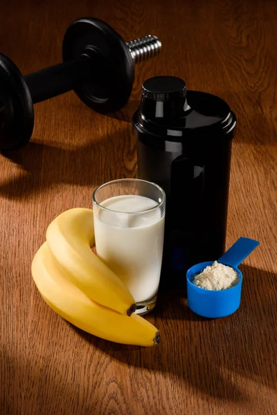 Batido de proteína com halteres e bananas na superfície de madeira — Fotografia de Stock