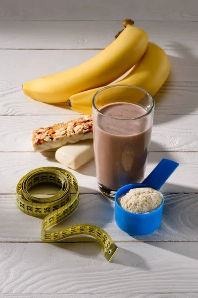 Bicchiere di frullato proteico con banane e barrette energetiche su tavolo di legno bianco — Foto stock
