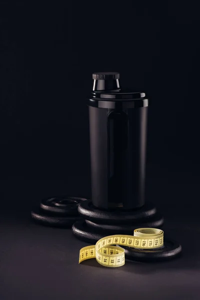 Protein container with measuring tape and weight plates isolated on black — Stock Photo