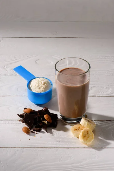 Glass of protein shake with almond, banana and chocolate on white wooden table — Stock Photo