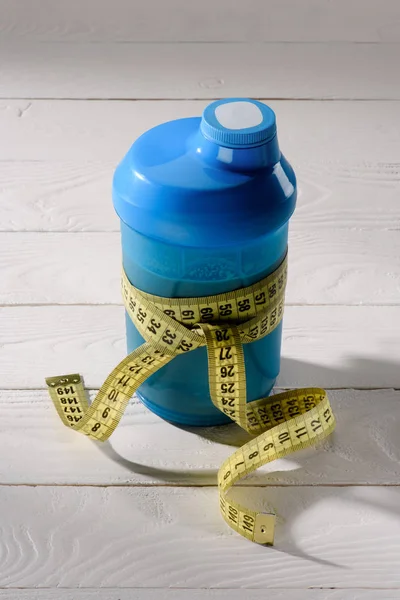 Close-up shot of protein shaker tied with measuring tape on white wooden table — Stock Photo