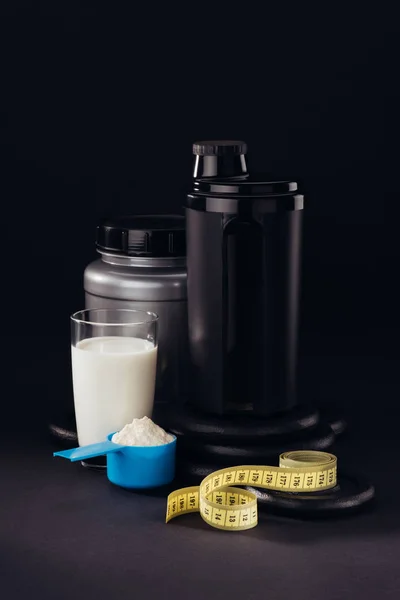 Protein shaker with glass of white liquid and measuring tape isolated on black — Stock Photo