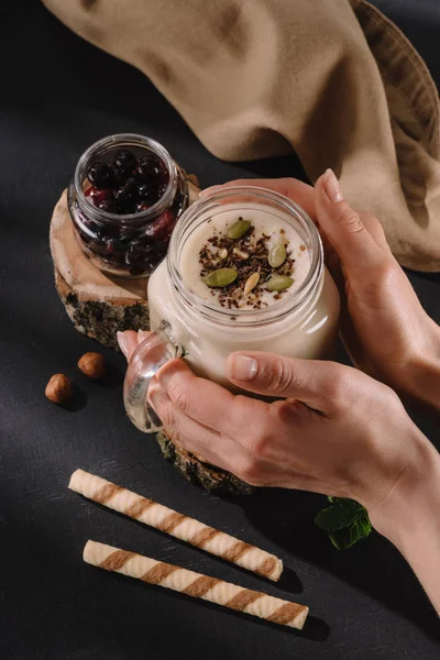 Cropped image of female holding milkshake with chocolate shaving and pistachio nuts, sweet straws, currants, walnuts and mint — Stock Photo