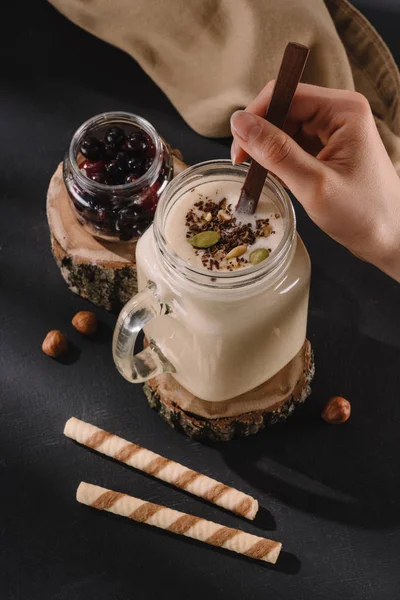 Cropped image of female mixing milkshake by spoon, currants, sweet straws and walnuts — Stock Photo